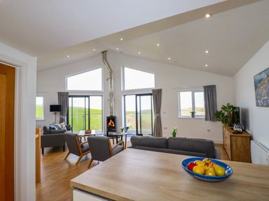 A living room with chairs a fireplace sliding glass doors and a bowl of fruit on a table at Jacana in Perranporth