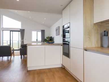 A kitchen and living area with white cabinets wood countertops and wooden floor at Jacana in Perranporth