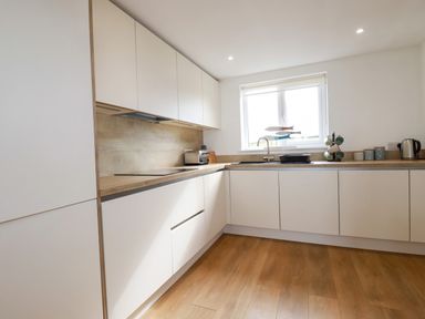 A kitchen with white cabinets wooden countertop and a window at Jacana in Perranporth