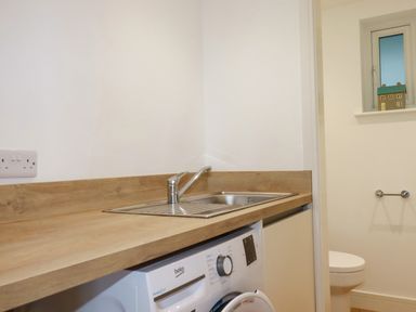 A wooden countertop with a sink faucet and a washing machine underneath next to a toilet in a small room at Jacana in Perranporth