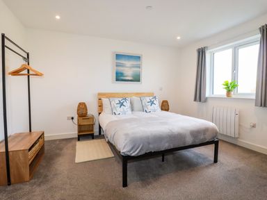 A bedroom with a double bed two bedside tables and a window with curtains at Jacana in Perranporth