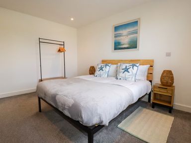 A bedroom with a bed with starfish pillows a wooden headboard a nightstand with a lamp a clothes rack with hangers and a painting on the wall at Jacana in Perranporth