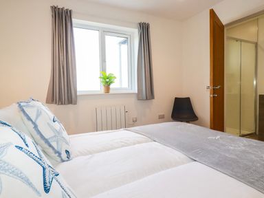 A bedroom with a bed featuring starfish pillows a window with curtains a plant and an open door leading to a bathroom at Jacana in Perranporth