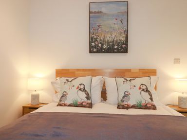 A bed with bird-themed cushions bedside tables with lamps and a painting above the headboard at Jacana in Perranporth
