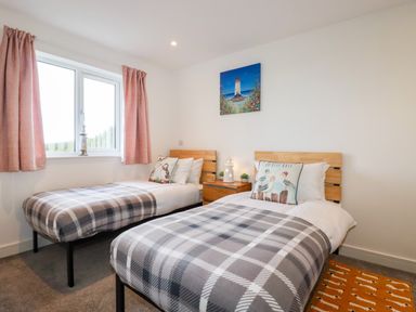 A bedroom with two single beds with plaid blankets and bird-themed pillows at Jacana in Perranporth