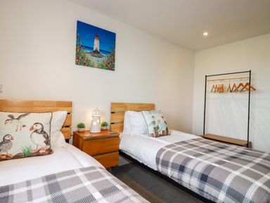 A bedroom with two single beds wooden headboards nightstand with lamp and plants coat rack with hangers at Jacana in Perranporth
