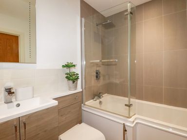 A bathroom with a bathtub and glass shower screen a sink with cabinet and a plant on the counter at Jacana in Perranporth