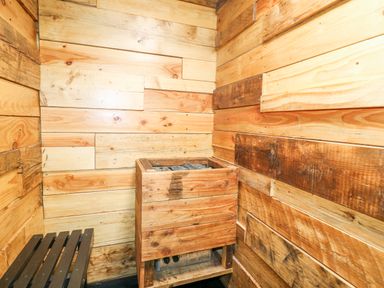 A small wooden room with a wooden heater containing sauna stones and a wooden bench at Orchard Retreat Staycation Kirton