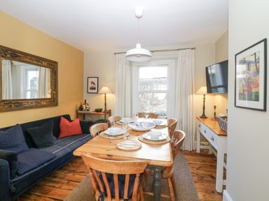 A dining room with a wooden table set for four chairs a blue sofa a large mirror and a window with white curtains at Springfield in Kingsand
