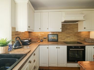 A kitchen with white cabinets wooden countertop a black stove and oven and brown tile backsplash at Springfield in Kingsand