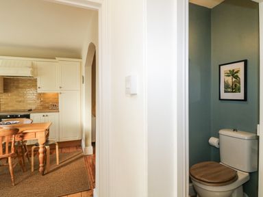 A kitchen with wooden chairs and table next to a small toilet with a framed picture at Springfield in Kingsand