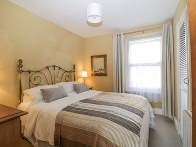 A bedroom with a metal bed frame a striped blanket two pillows a bedside table with a lamp a window with curtains and a wall mirror at Springfield in Kingsand