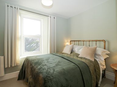 A bedroom with a bed covered in green bedding and pillows next to a window with curtains at Springfield in Kingsand