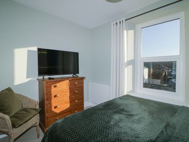 A bedroom with a chest of drawers and television next to a window with curtains and a chair at Springfield in Kingsand