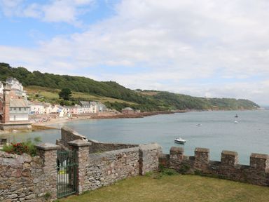 A coastal view with a stone wall in the foreground boats on the water and houses near a hillside at Springfield in Kingsand