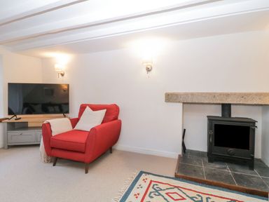 A room with a red armchair next to a wood stove and a television on a grey cabinet at Springfield in Kingsand