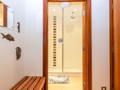 A bathroom with a shower and wooden bench at Heathcliffe House in Castleton near Cardiff