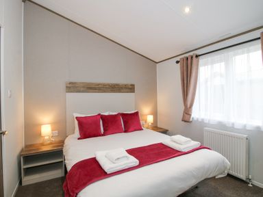 A bedroom with a double bed red cushions bedside tables lamps and window with curtains at Peony in Eardisland