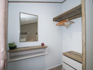 A corner of a room with a mirror above a wooden shelf and a closet with hangers and drawers at Peony in Eardisland