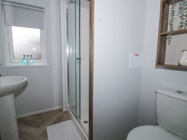 A bathroom with a shower cubicle toilet sink window and wooden wall shelves at Peony in Eardisland