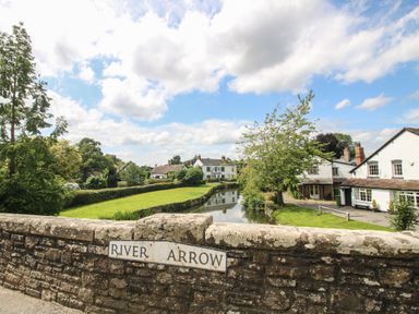 A stone bridge over the River Arrow with houses and trees in the background at Peony in Eardisland
