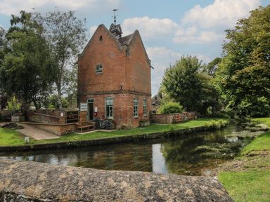 A brick building near a river with trees and benches at Peony in Eardisland