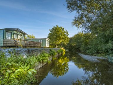A caravan by a river with a deck and a tree at Peony in Eardisland
