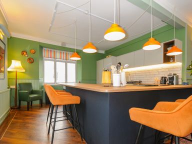 A kitchen with green walls orange pendant lights and bar stools at Sycamore Apartment in Lifton