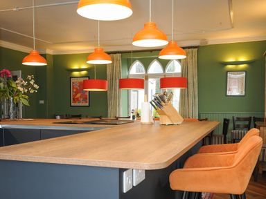 A kitchen island with orange chairs and pendant lights in a green walled room at Sycamore Apartment in Lifton