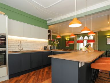 A kitchen with an island and orange pendant lights a wooden countertop and green walls at Sycamore Apartment in Lifton