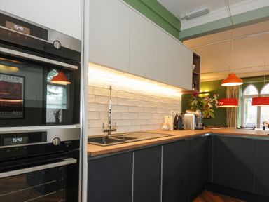 A kitchen with black and white cabinets a wooden countertop built in ovens a sink and pendant lights at Sycamore Apartment in Lifton