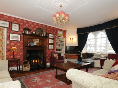 A living room with armchairs a fireplace a wooden coffee table a wall with framed pictures and a window seat with cushions at Sycamore Apartment in Lifton