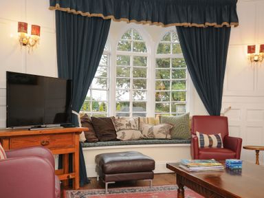 A living room with a television on a wooden stand a red armchair a window seat with cushions and dark curtains at Sycamore Apartment in Lifton