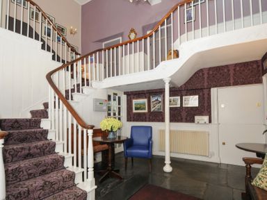 A stairwell with patterned carpet purple walls framed pictures a blue chair and wooden tables at Sycamore Apartment in Lifton