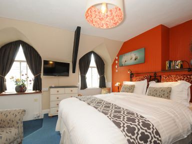 A bedroom with a large bed two windows with dark curtains a chest of drawers and a wall-mounted TV at Sycamore Apartment Lifton