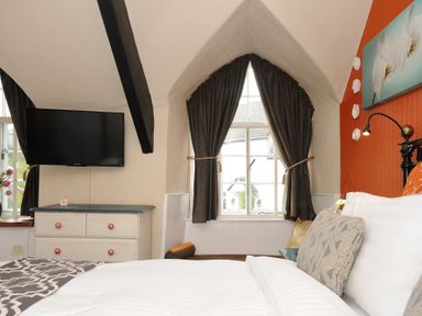 A bedroom with a bed next to a window with dark curtains and a dresser with a television above at Sycamore Apartment in Lifton
