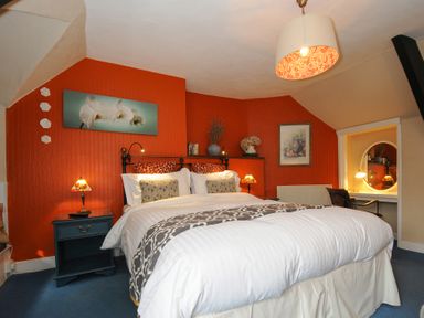 A bedroom with an orange accent wall a bed two bedside tables and a desk with a round mirror at Sycamore Apartment in Lifton