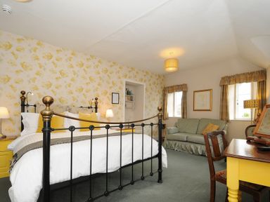 A bedroom with a black and brass bed a yellow desk green sofa and two windows at Sycamore Apartment in Lifton