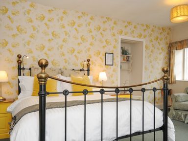 A bedroom with a metal bed frame yellow pillows bedside tables lamps floral wallpaper and an armchair at Sycamore Apartment in Lifton