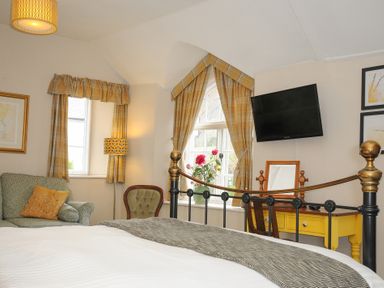 A bedroom with a bed a yellow desk a television armchair and windows with curtains at Sycamore Apartment in Lifton