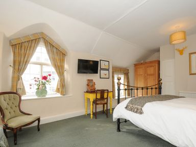 A bedroom with a bed a yellow desk a wooden chair an armchair and a wardrobe at Sycamore Apartment in Lifton