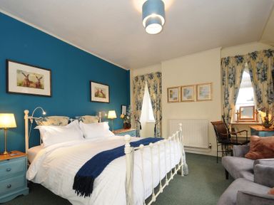 A bedroom with a double bed blue accent wall floral curtains bedside tables lamps and a seating area at Sycamore Apartment in Lifton