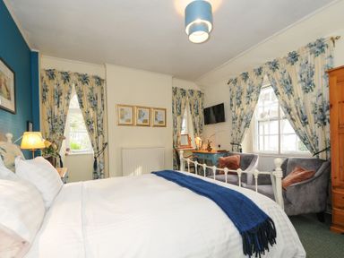 A bedroom with a bed a desk two armchairs floral curtains and a wall mounted television at Sycamore Apartment in Lifton