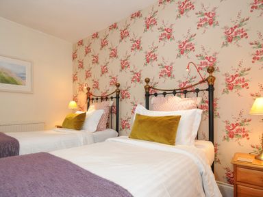 A bedroom with two single beds with floral wallpaper at Sycamore Apartment in Lifton