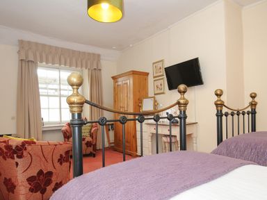 A bedroom with a metal bed frame purple bedding a wooden wardrobe armchair and a wall-mounted television at Sycamore Apartment in Lifton