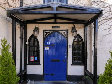 An entrance with a blue arched door and two arched windows with black frames at Sycamore Apartment in Lifton