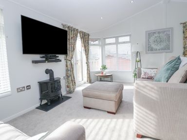 A living room with a wall-mounted TV stove beige sofas and a round side table at Swifts Reach Lodge Kirkstone 10 Limefitt Park near Windermere
