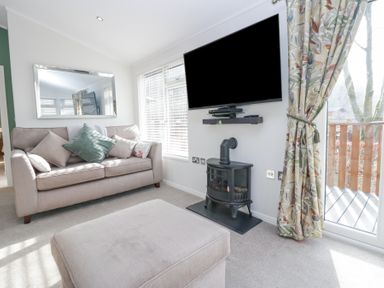 A living room with a sofa cushions a wall mounted television and a stove at Swifts Reach Lodge Kirkstone 10 Limefitt Park near Windermere