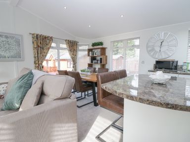 A living and dining area with sofa dining table chairs bookshelf and a kitchen counter at Swifts Reach Lodge Kirkstone 10 Limefitt Park near Windermere