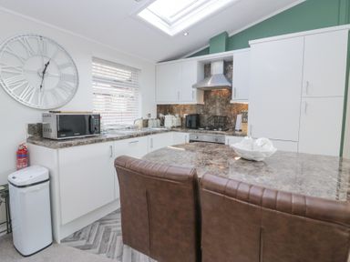A kitchen with white cabinets a microwave a stove and two brown chairs at Swifts Reach Lodge Kirkstone 10 Limefitt Park near Windermere